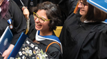 Students standing in caps and gowns smile and talk at Commencement